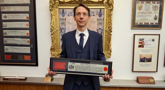 Image shows Professor Germond with a framed copy of the Freedom at Guildhall against a backdrop of other framed items
