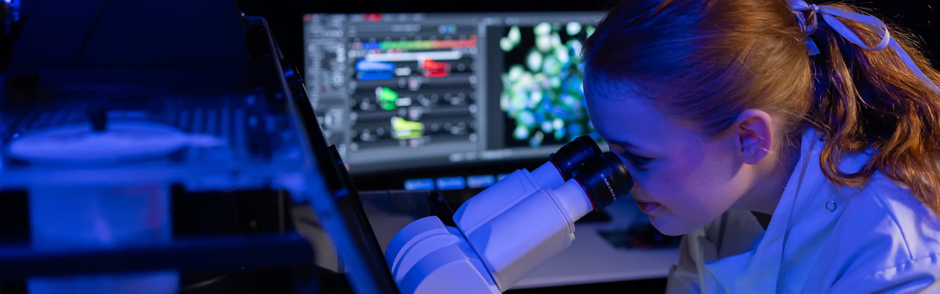 Student looking into a microscope in a darkened lab