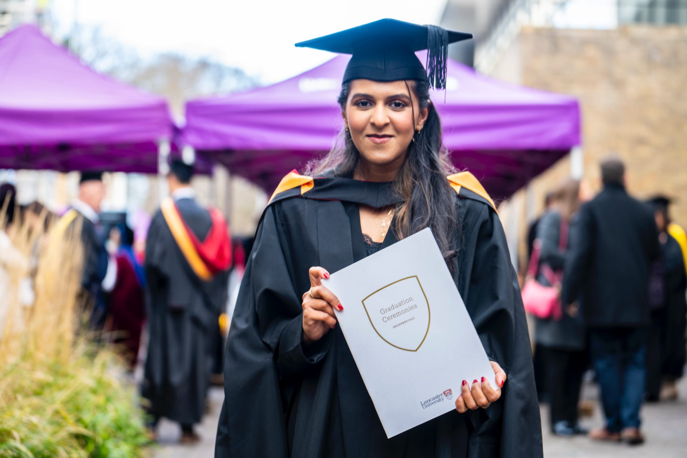 A smiling graduate holding a graduation programme 