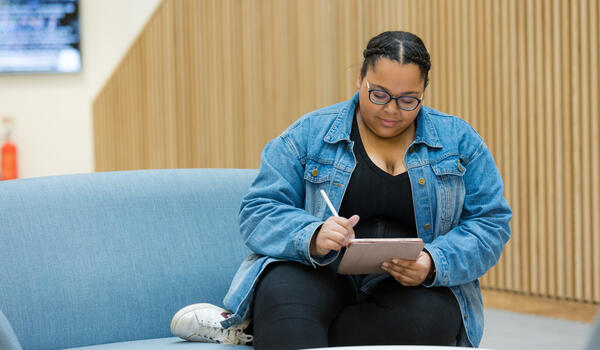 Student taking notes on a tablet computer while sitting on a blue sofa 