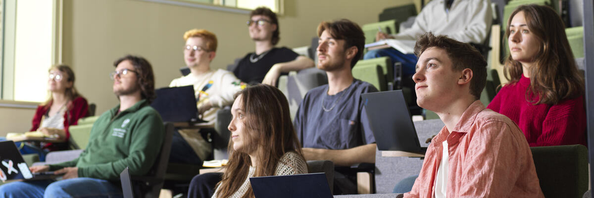 Students sit in rows in a lecture theatre and pay attention.