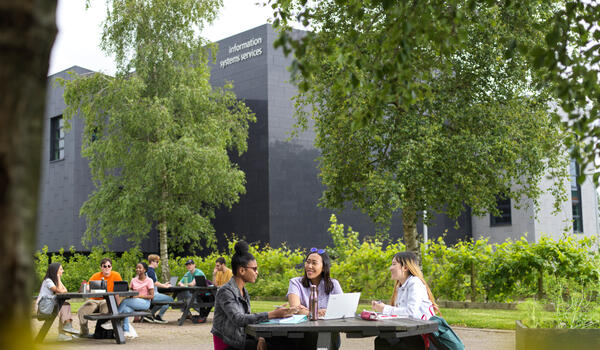 Students sat on a picnic bench on campus in front of ISS building