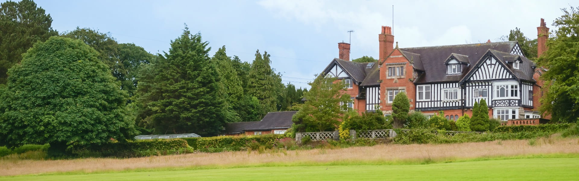 A Victorian mock Tudor house sits on the ridge of a hill, surrounded by trees and fields.