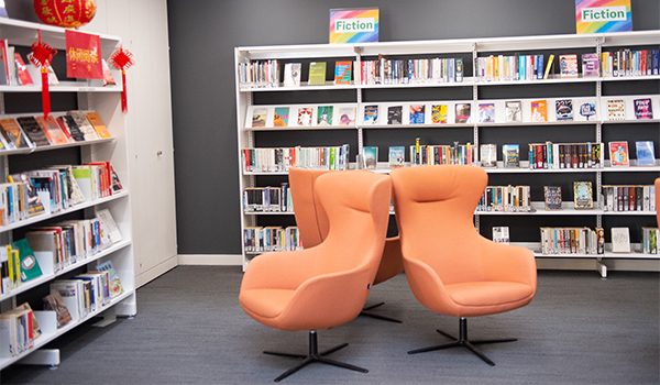 Leisure reading area with comfortable reading chairs with shelves of fiction books.