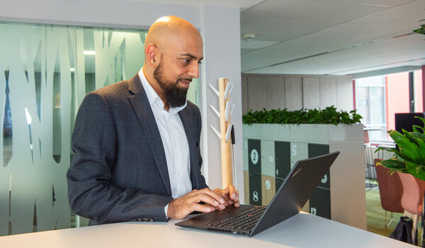 A smartly dressed man works at a laptop in a modern office building