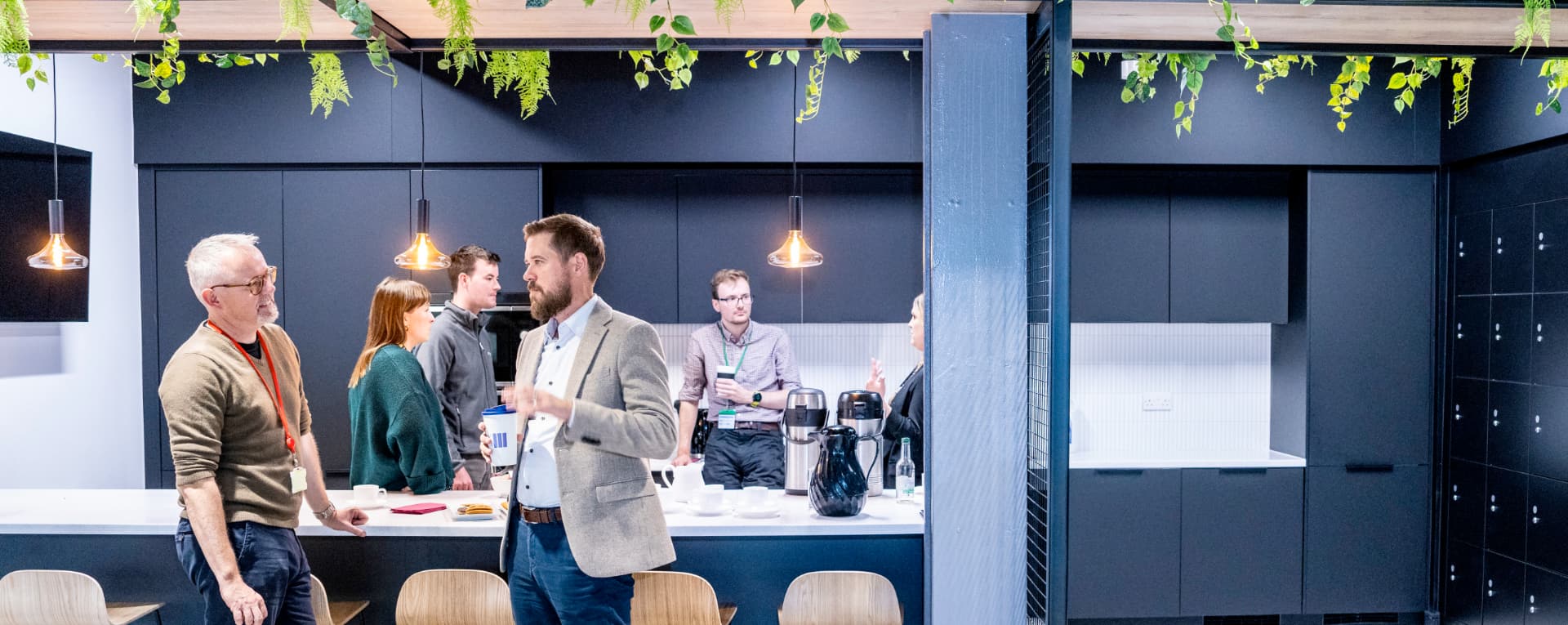 Several people standing in an office kitchen, engaged in discussion