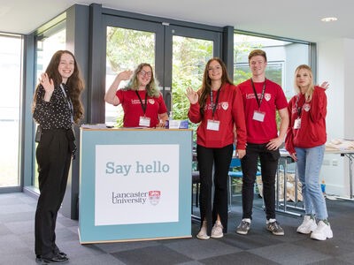 One staff member and four Student Ambassadors in red branded hoodies waving at the camera. 