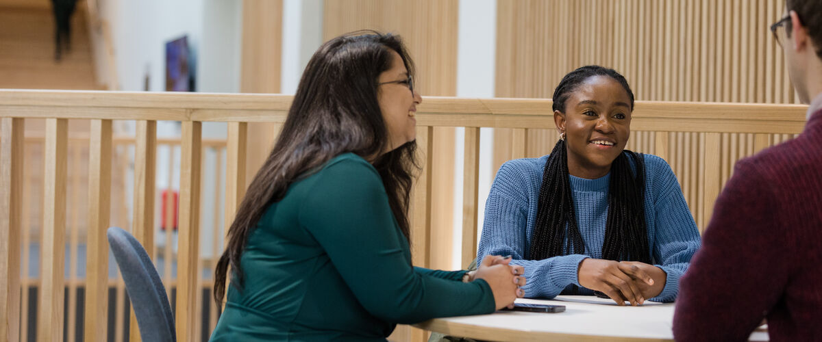Three students sit at a desk on a mezzanine overlooking a wood panelled atrium.