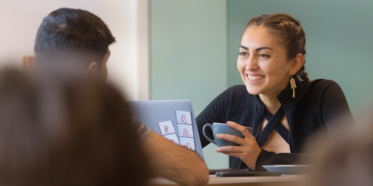 A student sits drinking a coffee and smiling