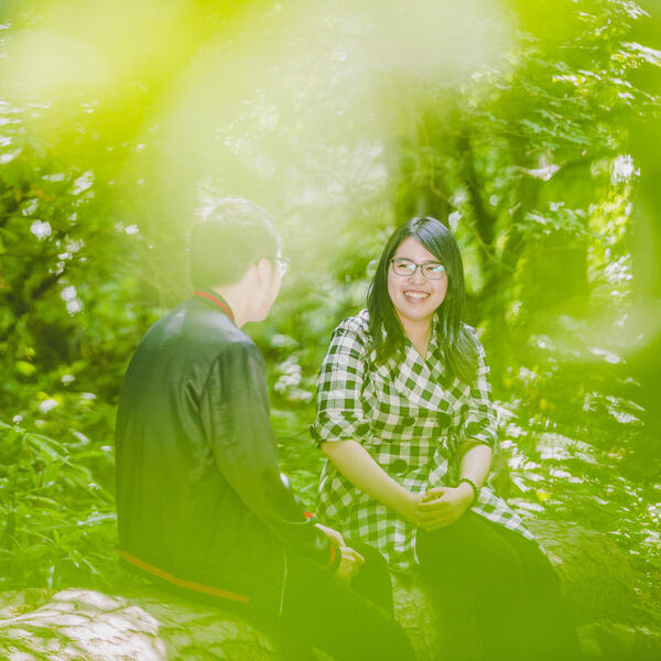 Two students sitting on a log, talking amongst the trees.