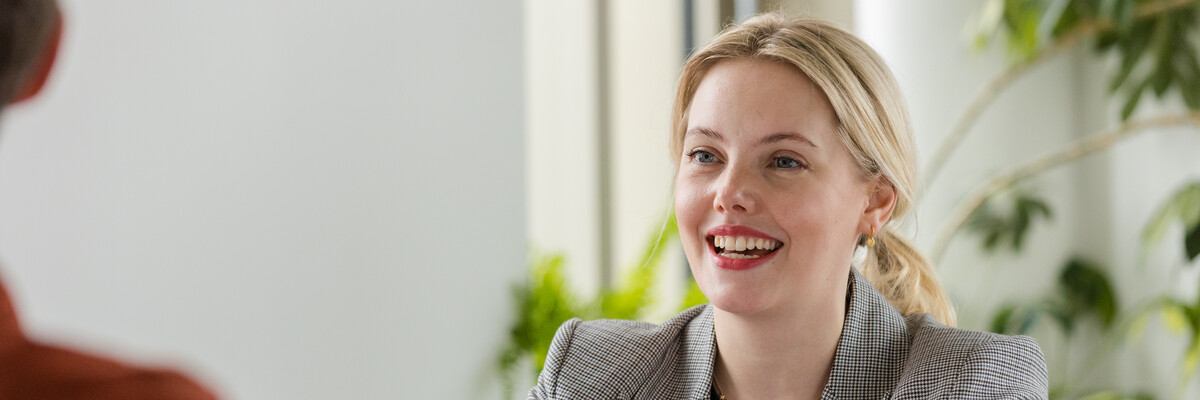 A member of staff sits at a desk in a brightly lit office with plants in the background.