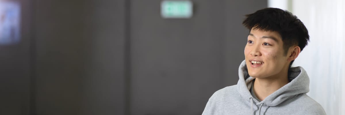 A student smiles and looks to the left. They are in a well-lit, grey room.