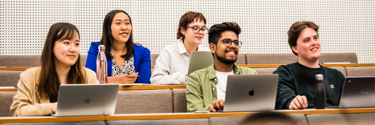 Two rows of students sit smiling in a lecture.