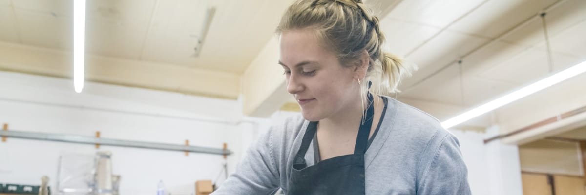 A student wearing an apron works in a workshop