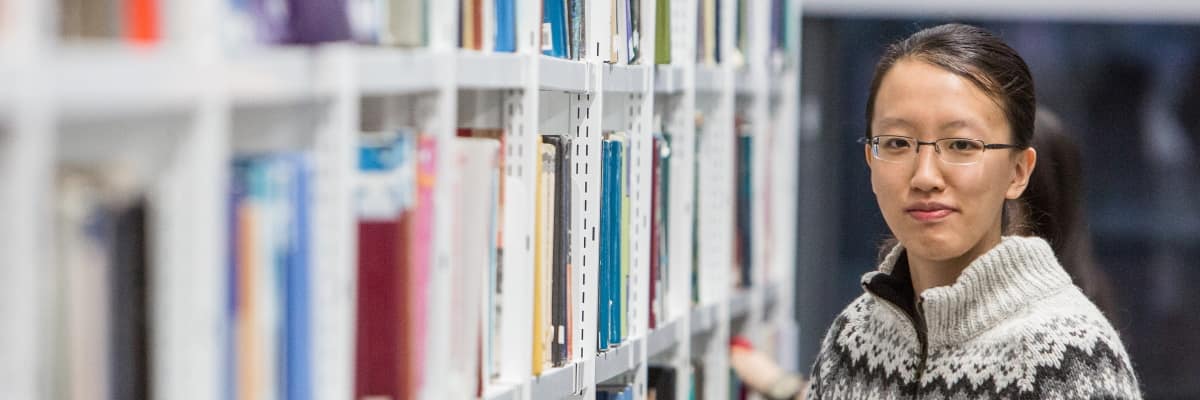 A student in the library looks down an aisle towards the camera
