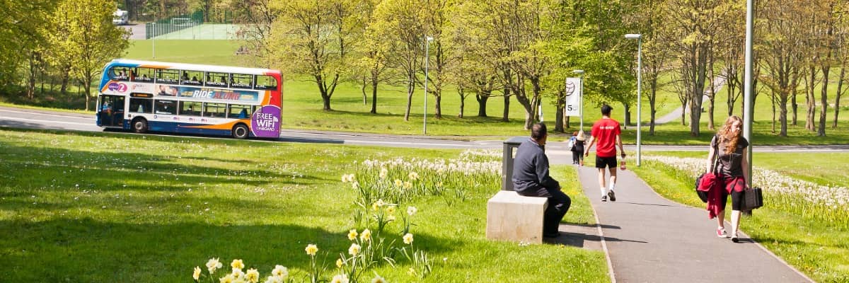 Students walking up the hill with a bus in the background.