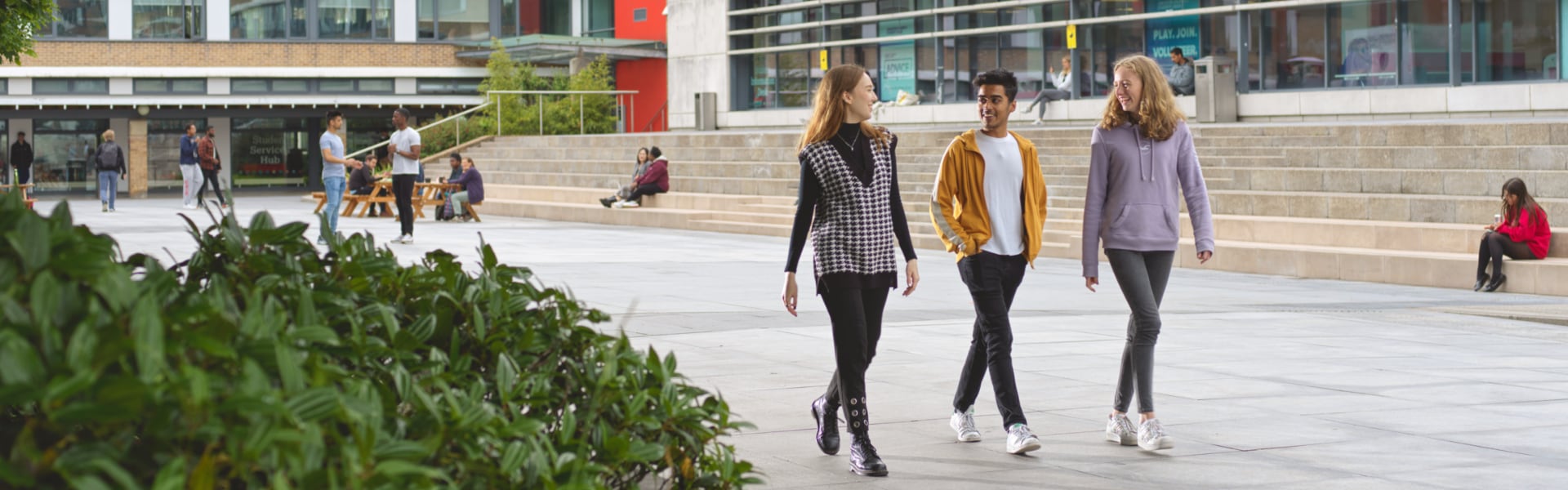 Three students walk confidently across a paved square at Lancaster University